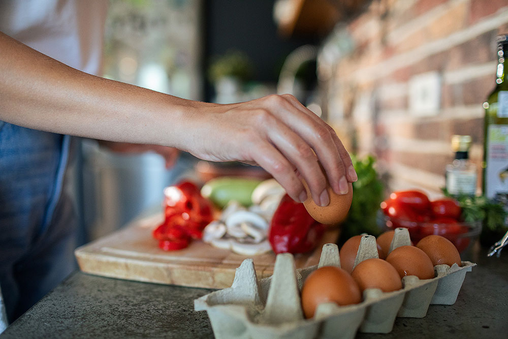 Woman cracking an egg in the kitchen while preparing a healthy breakfast.