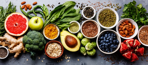 A variety of fruits, vegetables, seeds, superfoods, cereals, and leafy vegetables arranged on a gray concrete background.