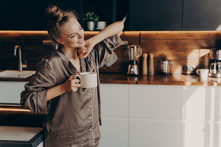 Young woman smiling and stretching after getting good sleep thanks to proper sleep hygiene.