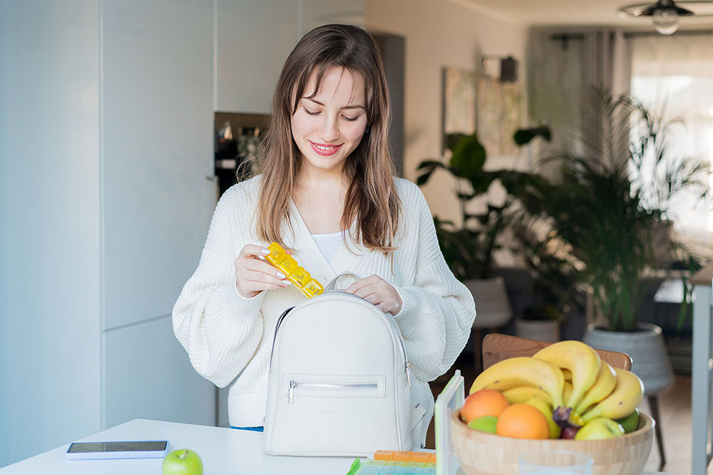 Woman placing a daily pill organizer into her bag.