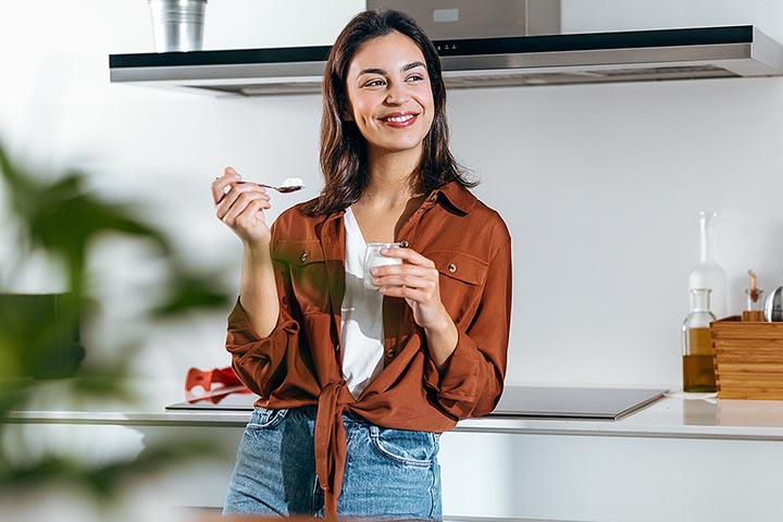 Woman enjoying yogurt while standing in the kitchen.