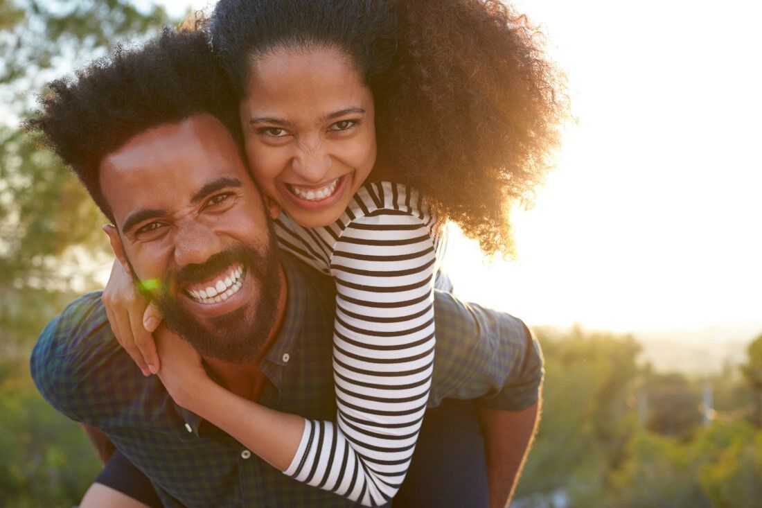 A woman enjoys a sunny day with a piggyback ride on a man's back.